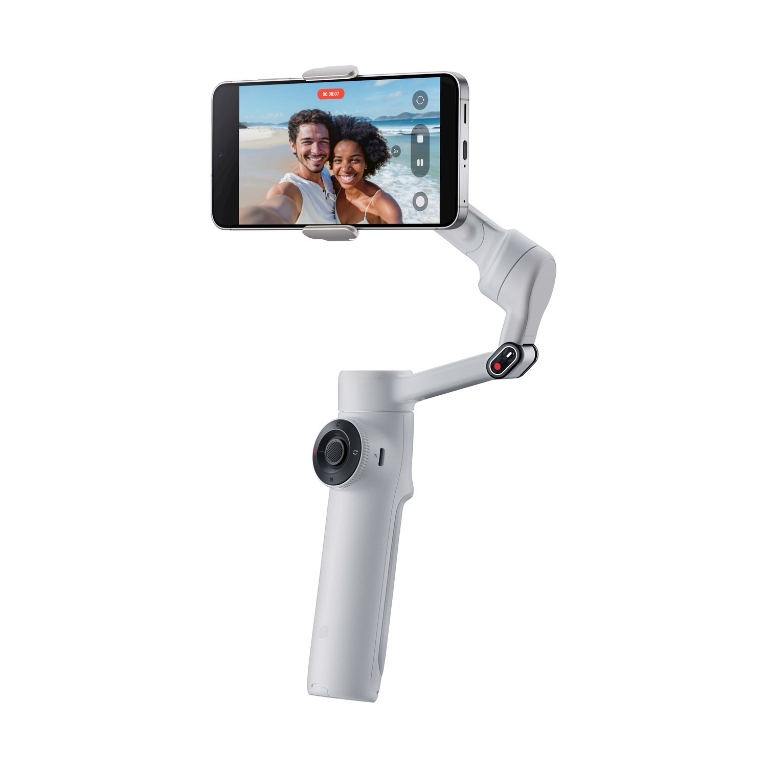 Un gimbal bianco tiene un telefono che mostra una coppia su una spiaggia. Il gimbal è bianco, con un quadrante di controllo e un'impugnatura.