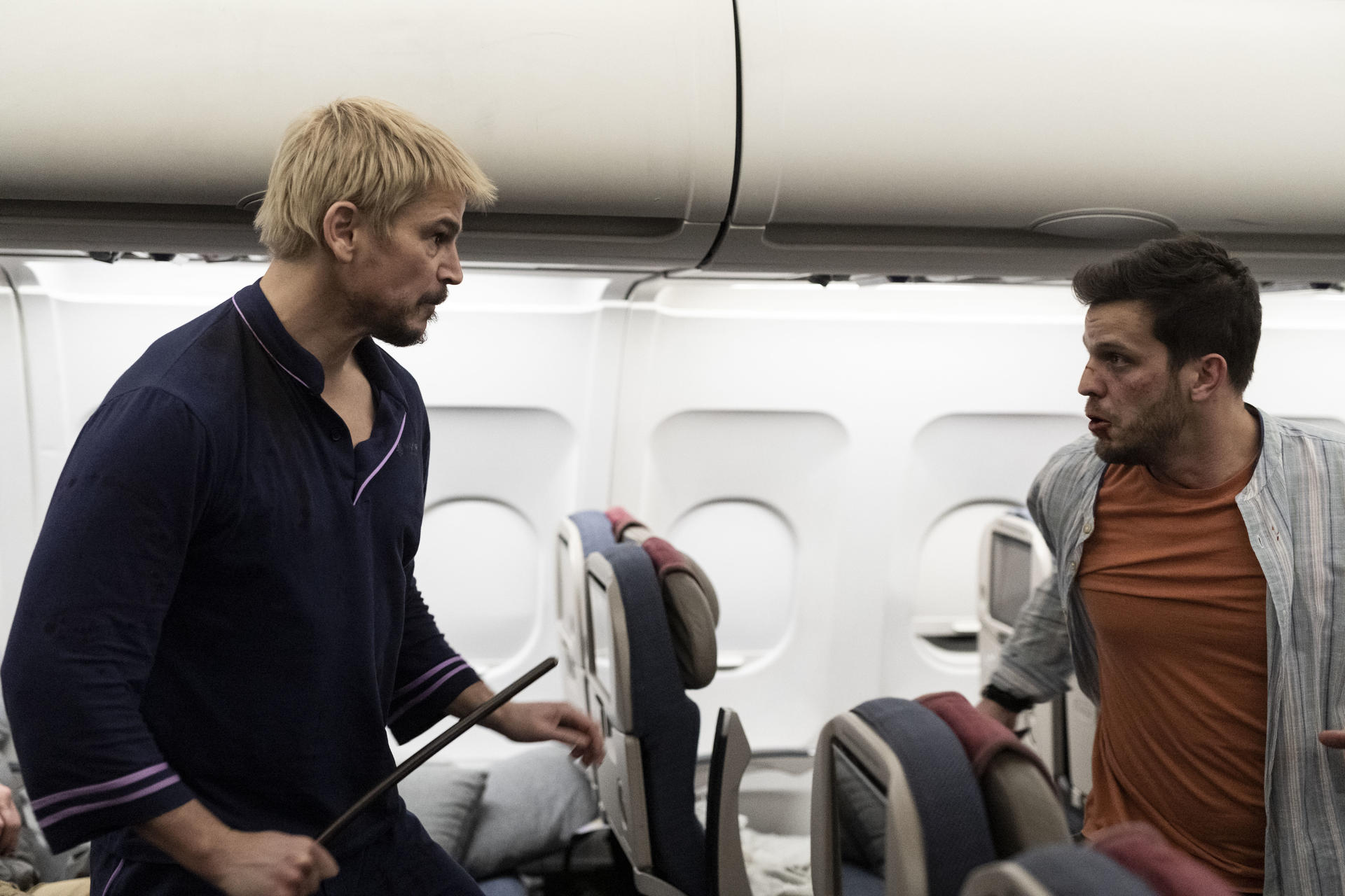 Zwei Männer stehen in einer Flugzeugkabine zwischen den Sitzen.