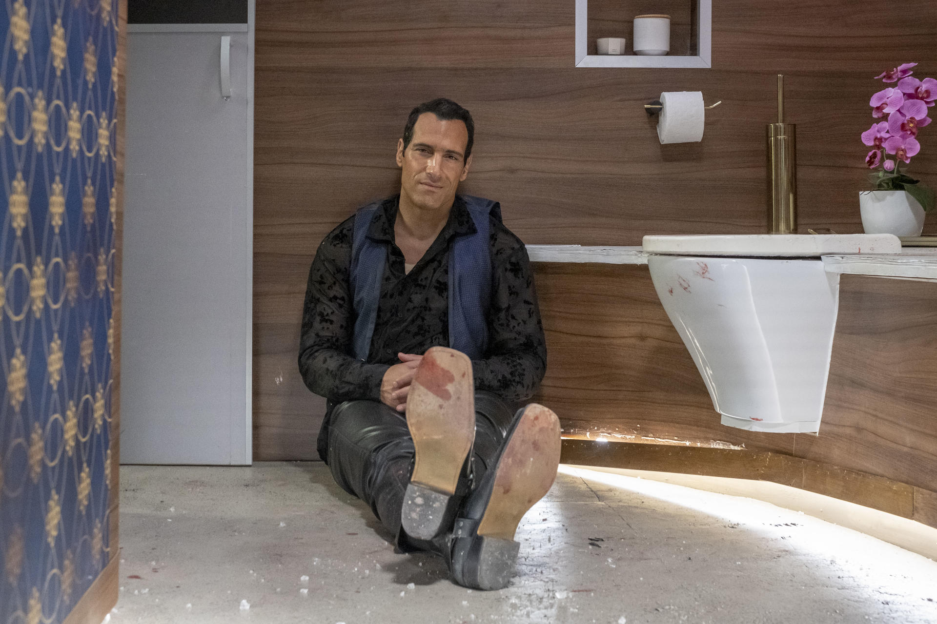 Mann sitzt auf dem Boden im Bad mit Toilette und Orhidee.
