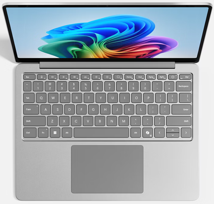 Egy ezüst laptop, kinyitva, hogy egy színes absztrakt képet mutasson a képernyőn. A billentyűzet és az érintőpad látható.