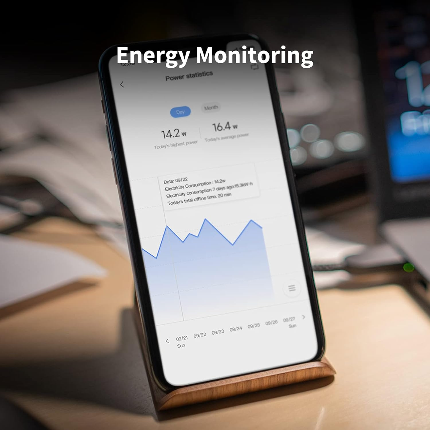 Egy telefon energiafigyelő alkalmazást jelenít meg teljesítmény statisztikákkal és egy vonaldiagrammal. A telefon egy fa állványon nyugszik.