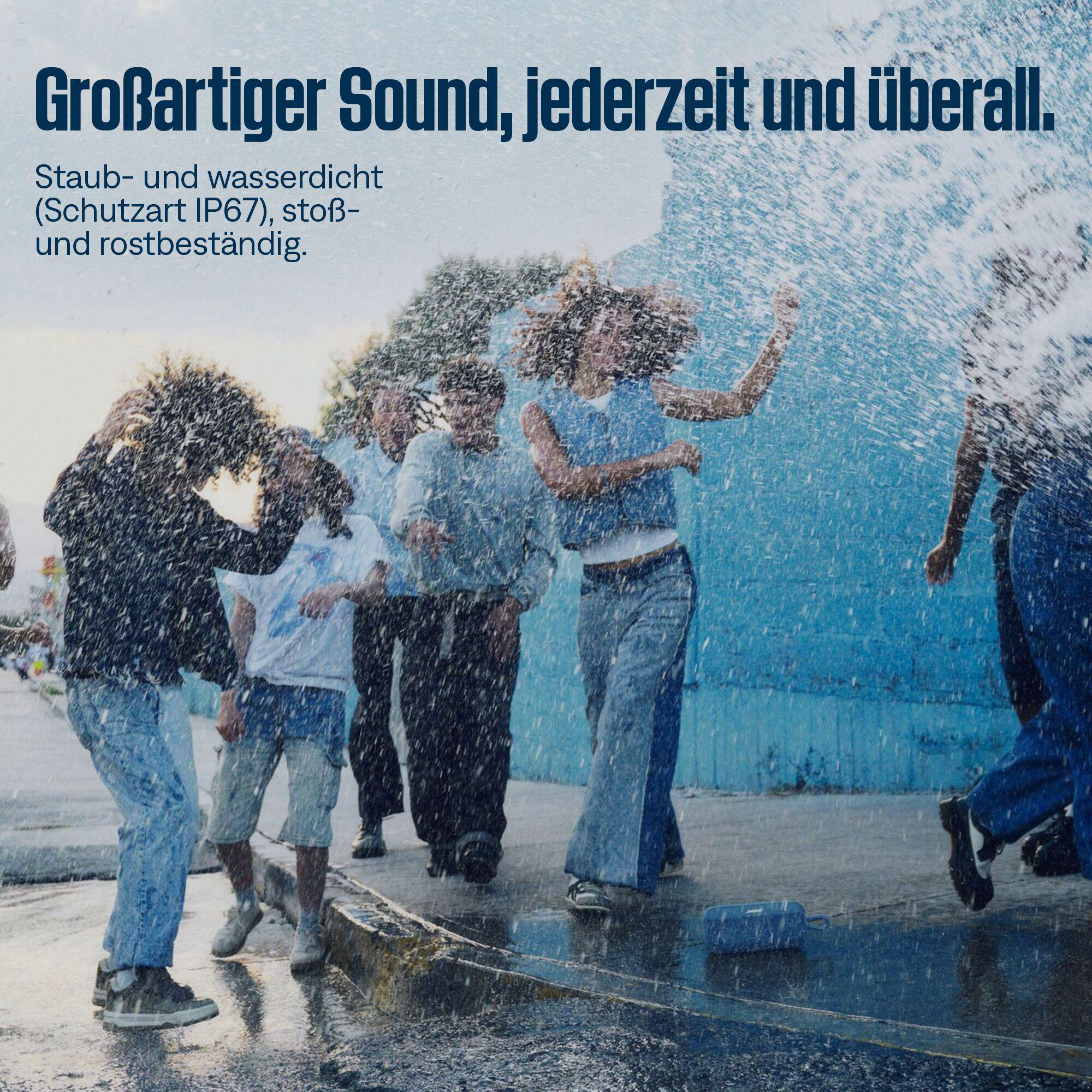 Menschen tanzen im Regen. Sie tragen Freizeitkleidung. Der Hintergrund ist eine blaue Wand.