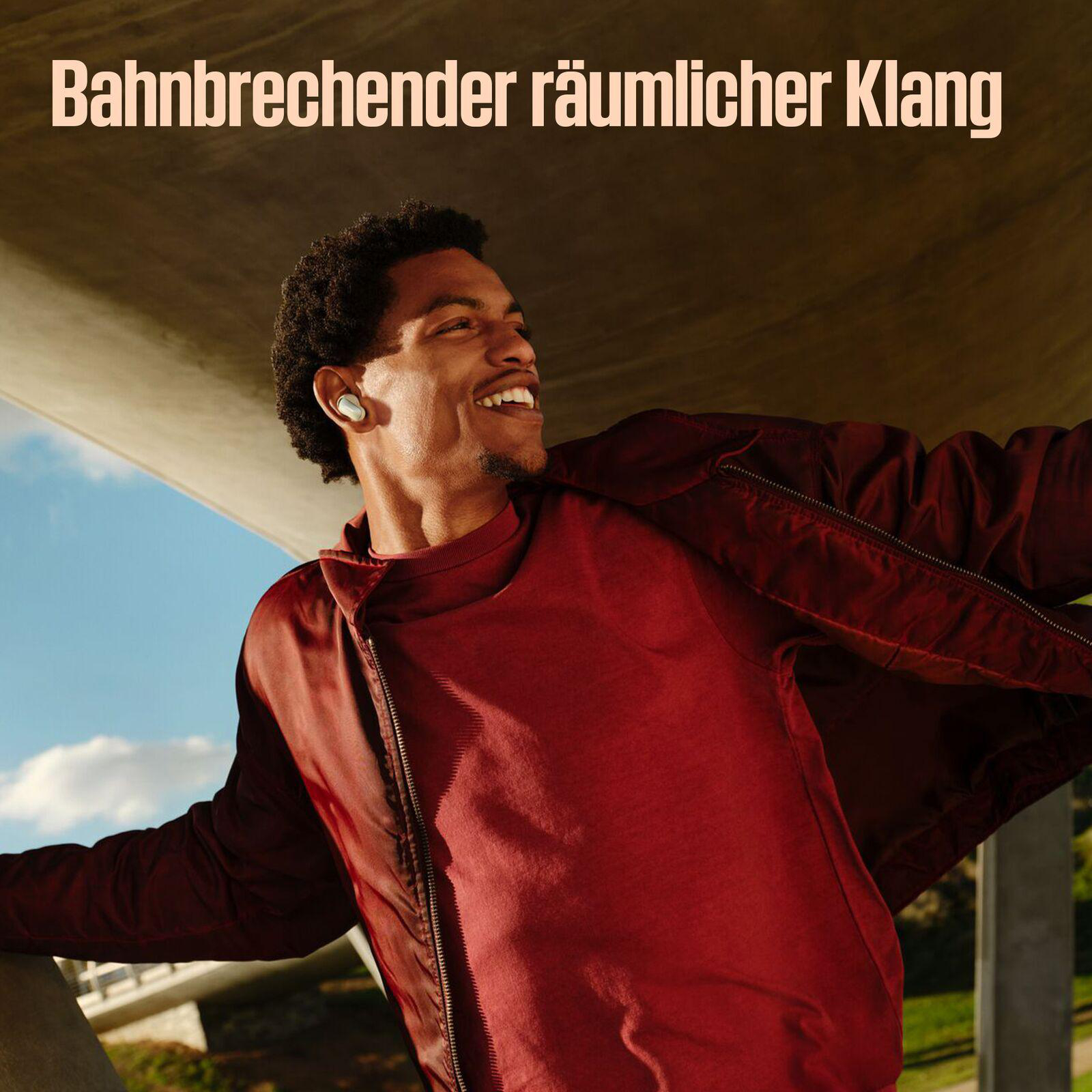 Ein lächelnder Mann mit roter Jacke und Ohrhörern. Oben steht: Bahnbrechender räumlicher Klang.