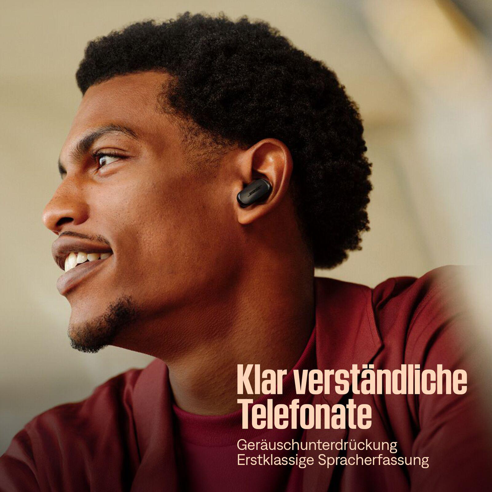 Ein lächelnder schwarzer Mann trägt einen Ohrhörer. Text sagt "Klare Telefonate". Er trägt ein rotes Hemd, der Hintergrund ist beige.