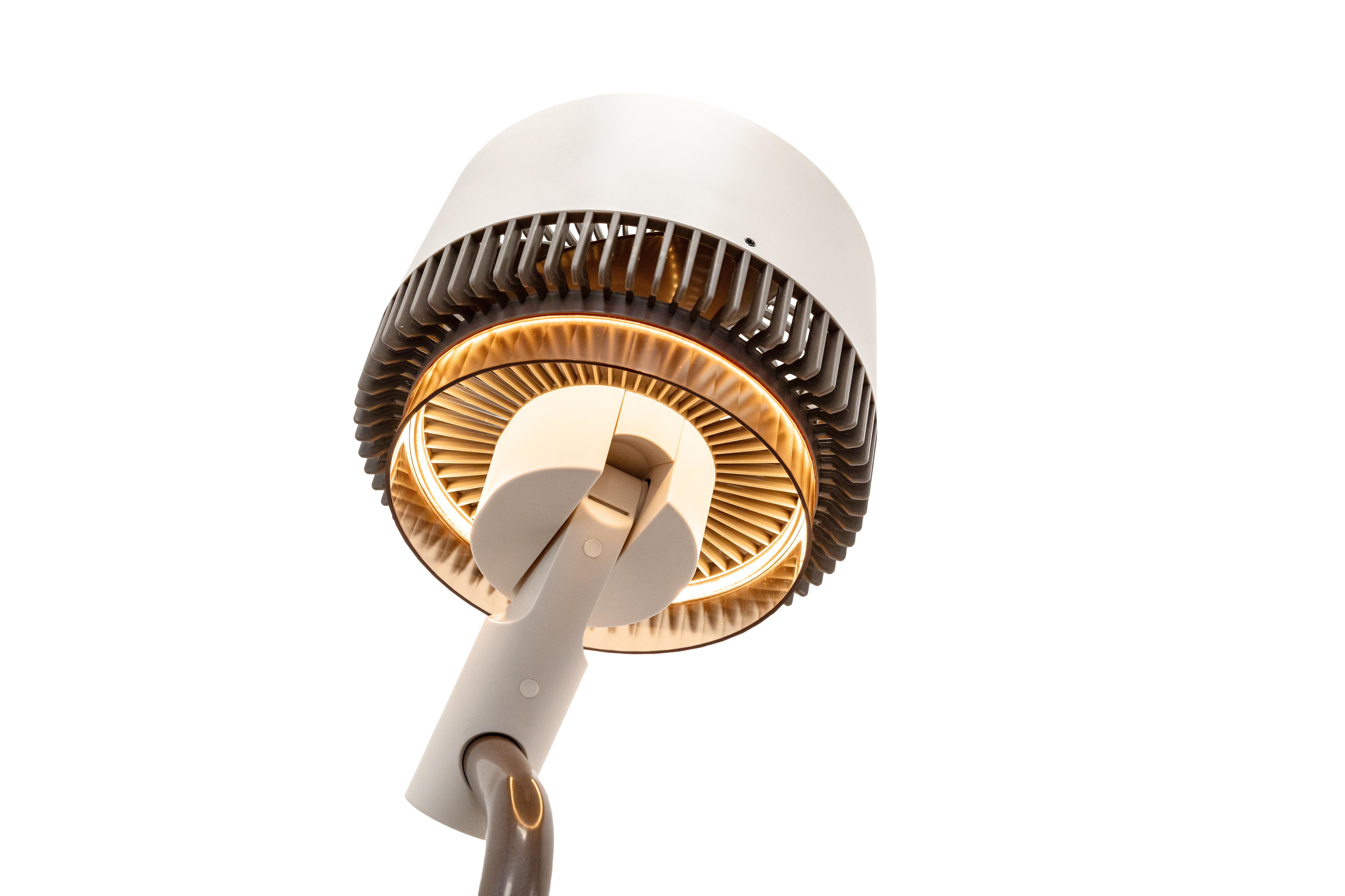 Eine moderne Lampe mit weißem Schirm, dunkelgrauen Lamellen und einer goldgelben Lichtquelle vor weißem Hintergrund.