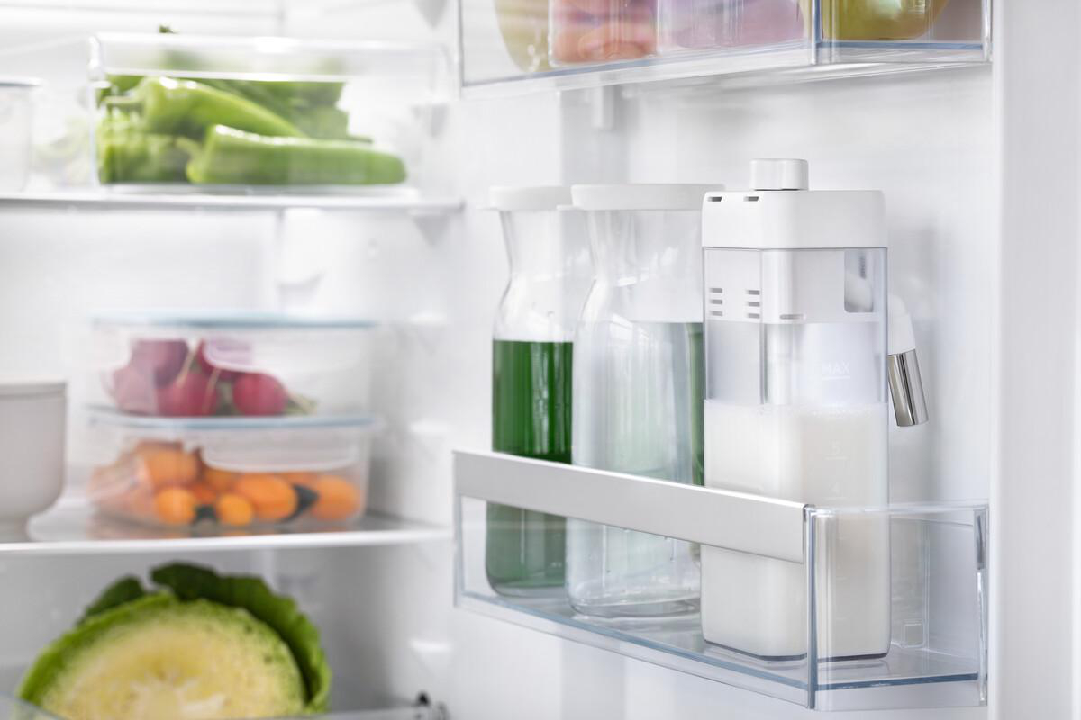 Im Kühlschrank. Grüne Paprika, Radieschen, Karotten und ein Salatkopf sind zu sehen. Milch und Saft in Glasbehältern.