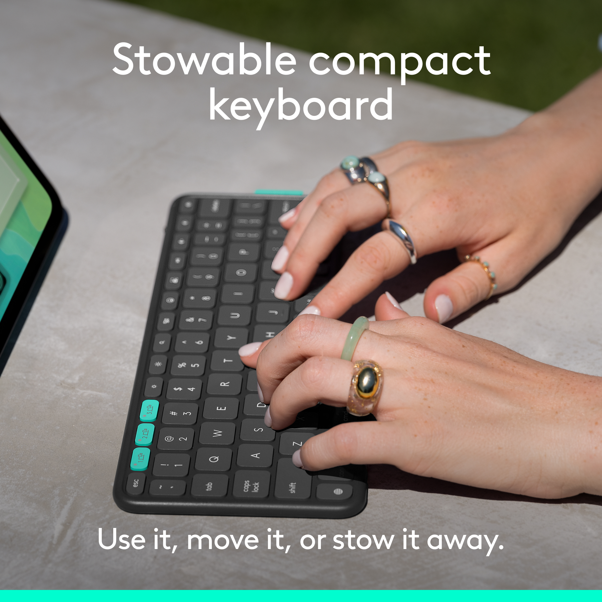 Hände tippen auf einer schwarzen Tastatur. Ringe schmücken die Finger. Die Tastatur liegt auf einer grauen Oberfläche.