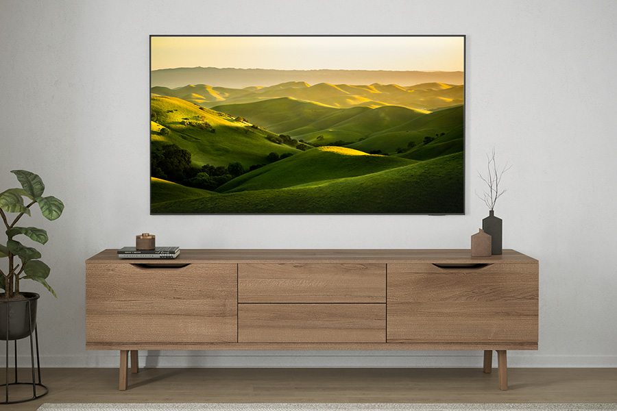 Fernseher mit grüner Hügellandschaft. Er befindet sich über einem Holzschrank mit Dekoration und einer Pflanze.