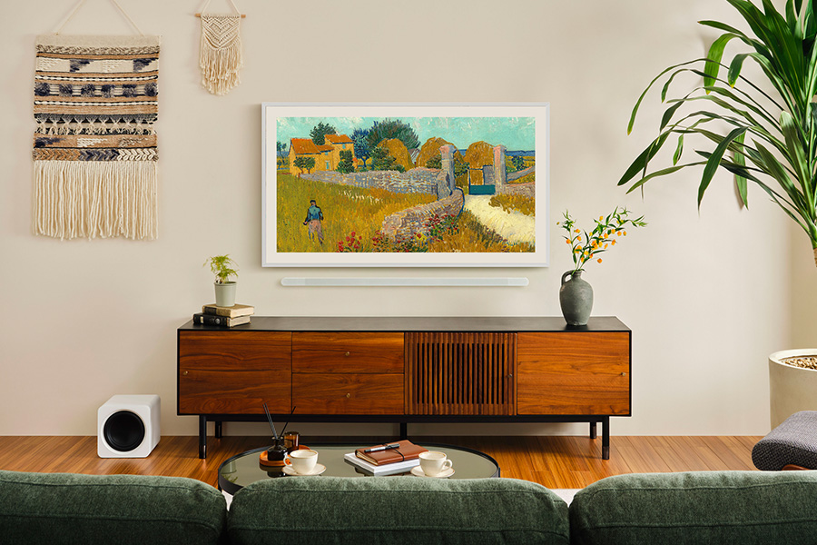 Soggiorno con dipinto in TV. Visibili un mobile in legno, un subwoofer bianco, un divano verde e una pianta.