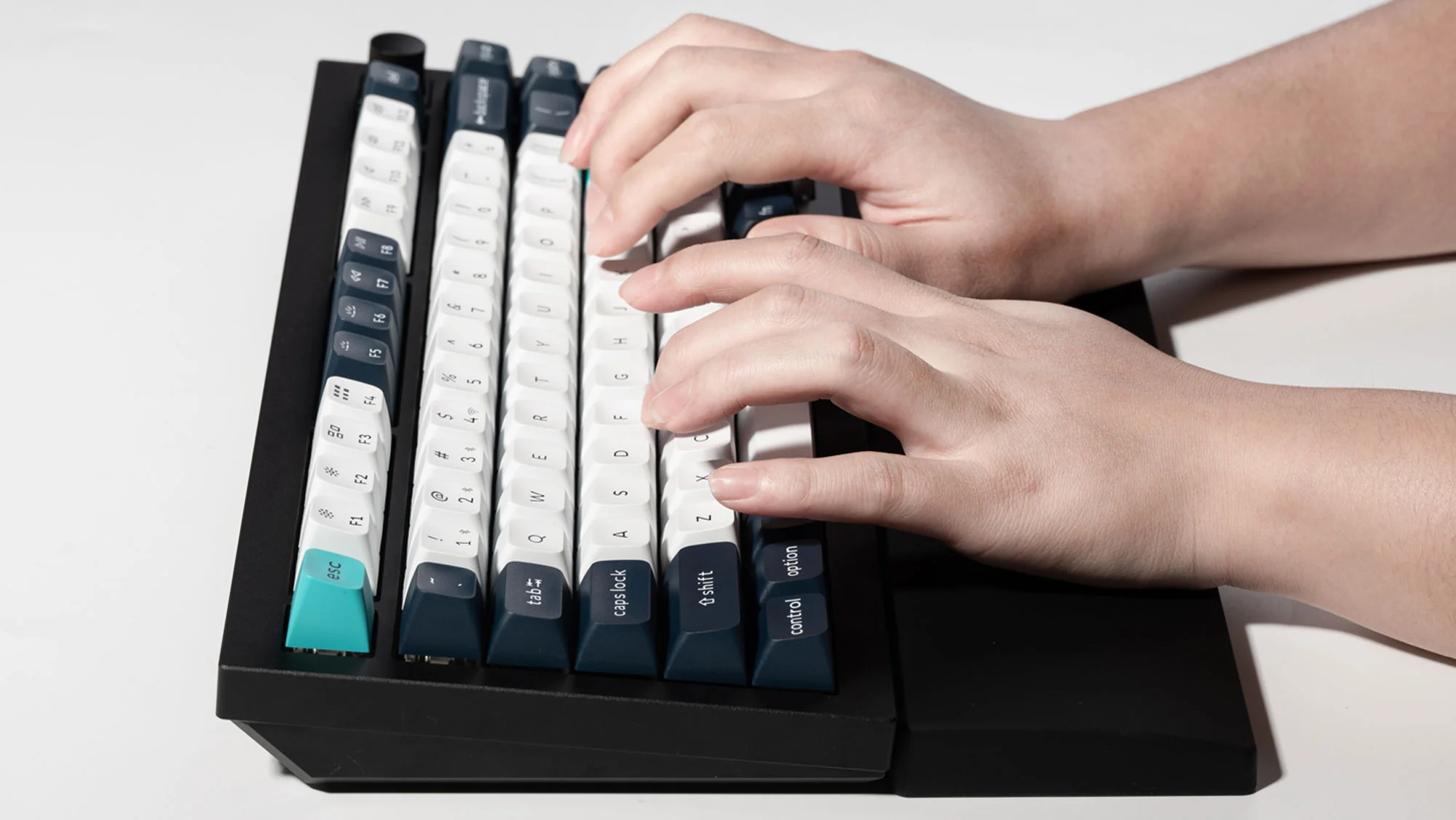 Mani che digitano su una tastiera meccanica in bianco e nero. I tasti sono bianchi con lettere nere. Lo sfondo è bianco.