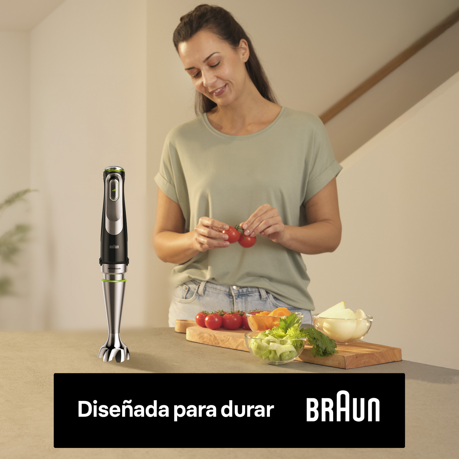 Mujer en la cocina con batidora Braun. Tomates, apio y cebollas en la mesa. La batidora está en primer plano.