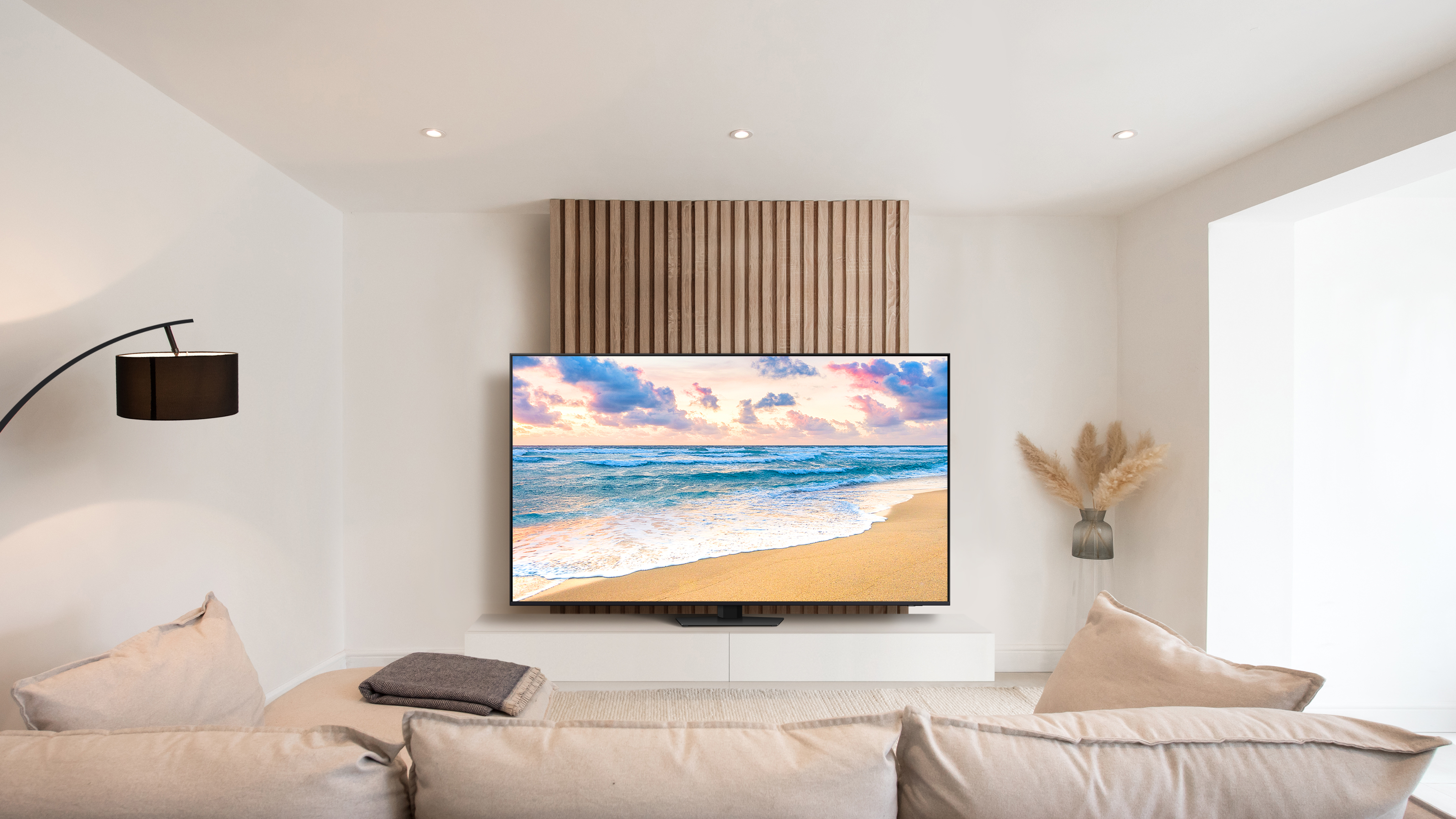 Wohnzimmer mit Strandblick-TV, beigem Sofa und Stehlampe. Neutrale Farben dominieren den Raum.