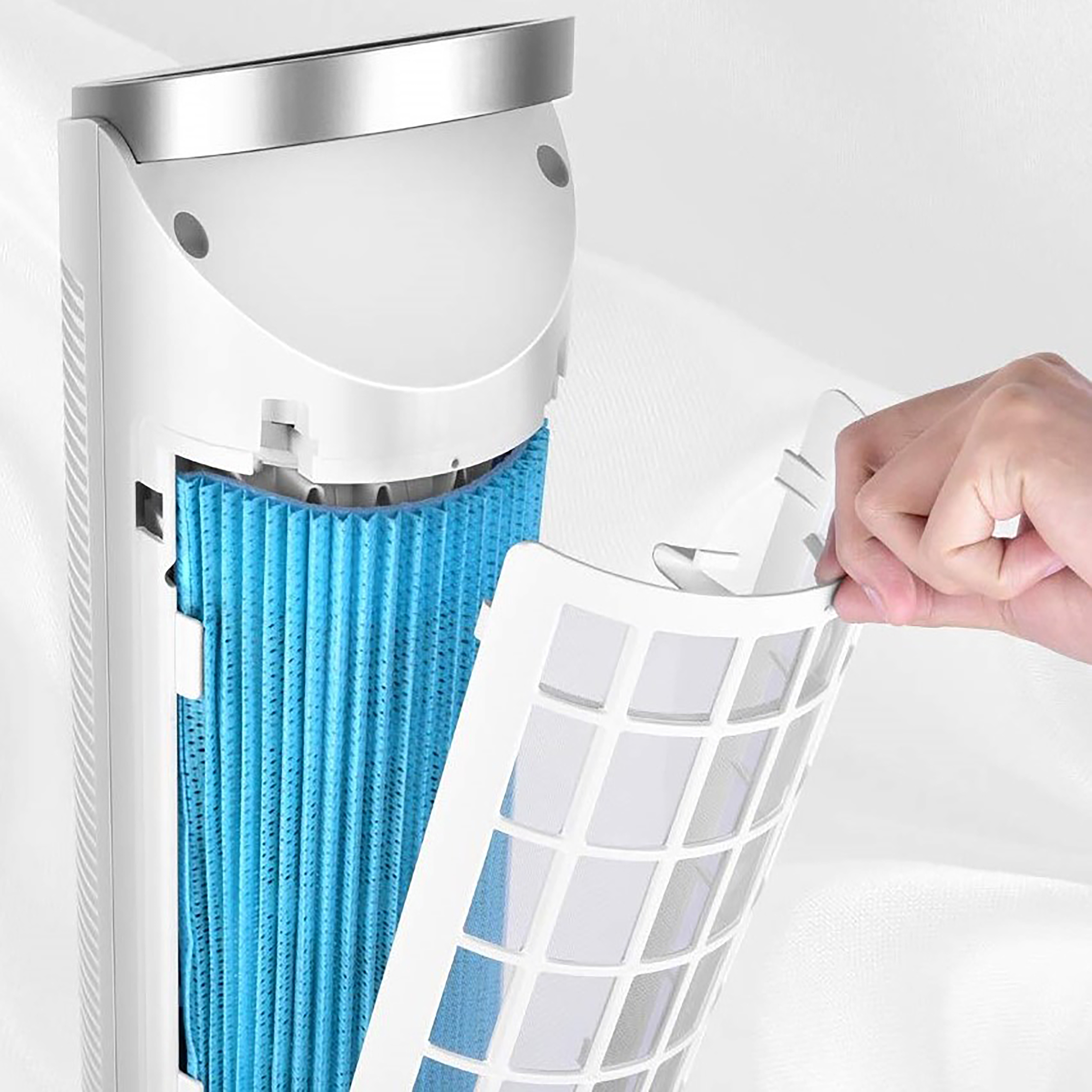 Eine Hand entfernt einen weißen Filter aus einem weißen Luftreiniger. Blaues Filtermaterial ist im Inneren zu sehen.