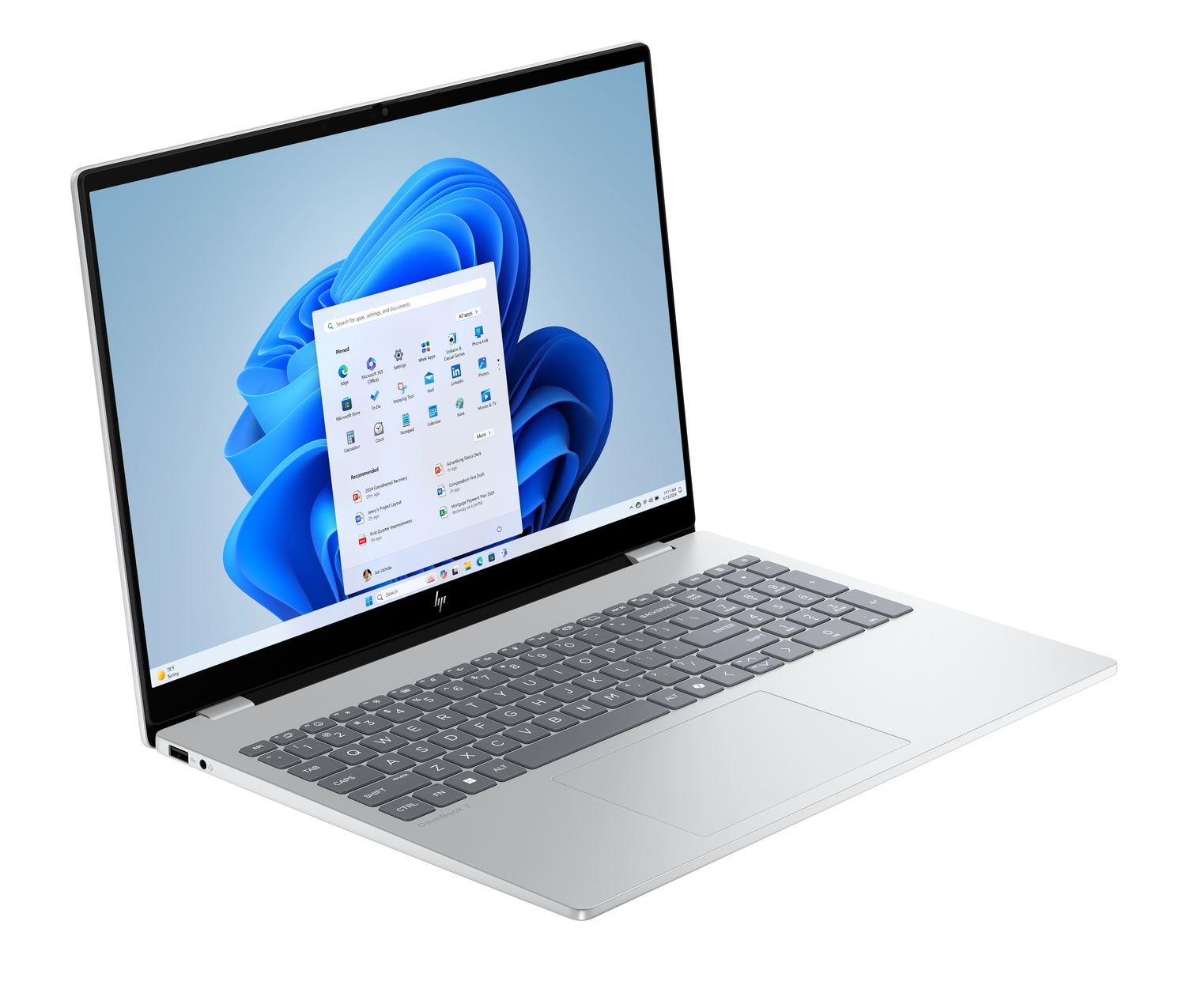 Un portátil HP plateado está abierto, mostrando el escritorio de Windows 11. La pantalla muestra el menú de inicio. El teclado es visible.