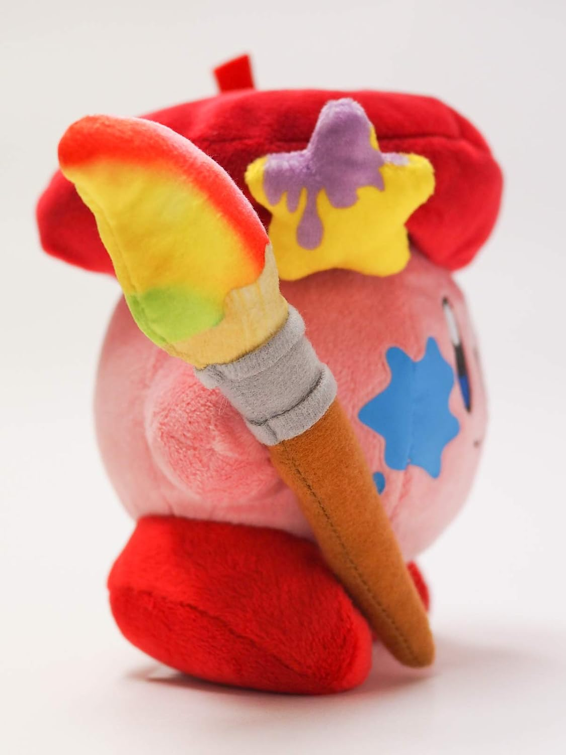 Ein rosa Kirby-Plüschtier mit roter Baskenmütze und Pinsel. Es hat einen Stern auf dem Hut und einen blauen Farbfleck.