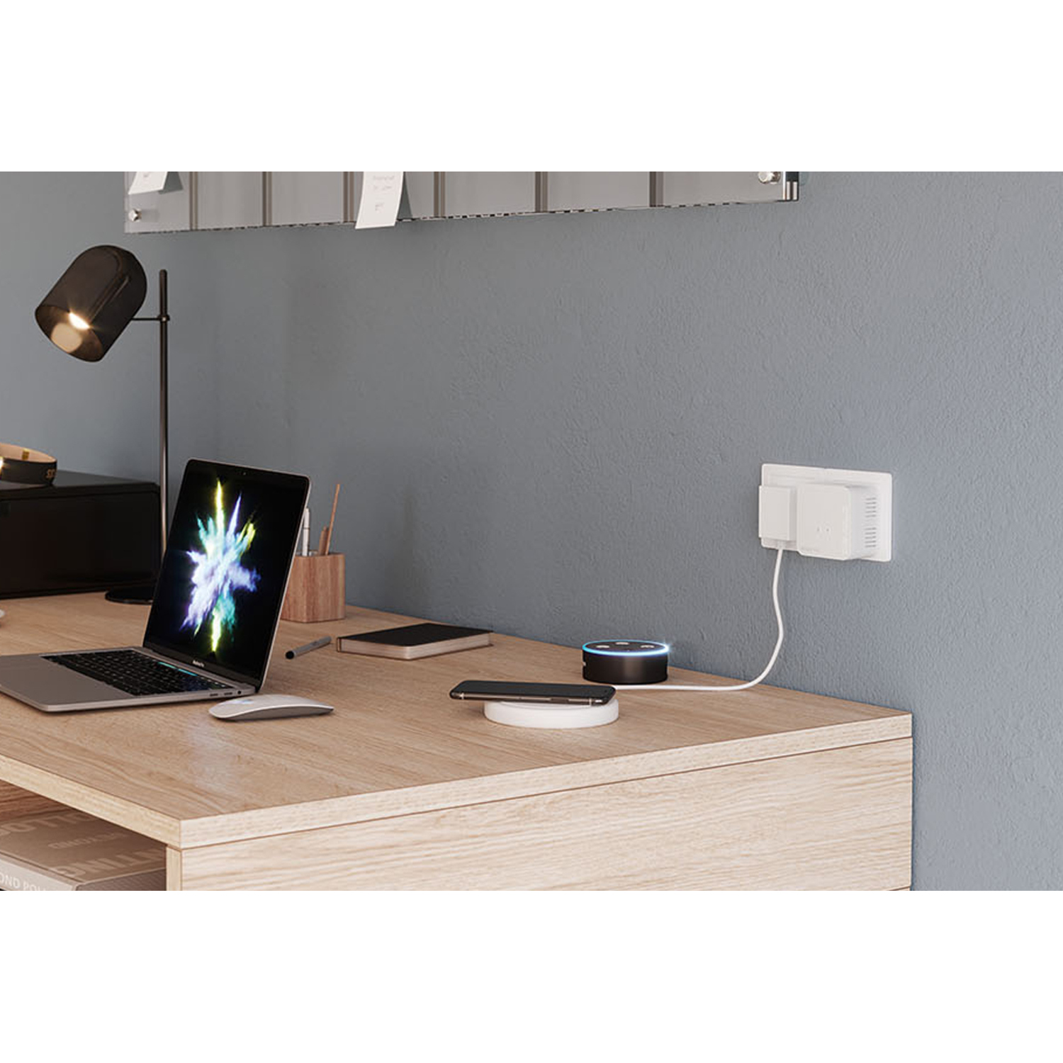 Un bureau avec ordinateur portable, souris, lampe, haut-parleur intelligent, téléphone et prise de courant. Mur gris en arrière-plan.