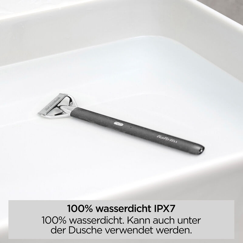 Ein schwarzer und silberner Rasierer liegt in einem weißen Waschbecken mit Wasser. Der Text unten besagt, dass es wasserdicht ist.