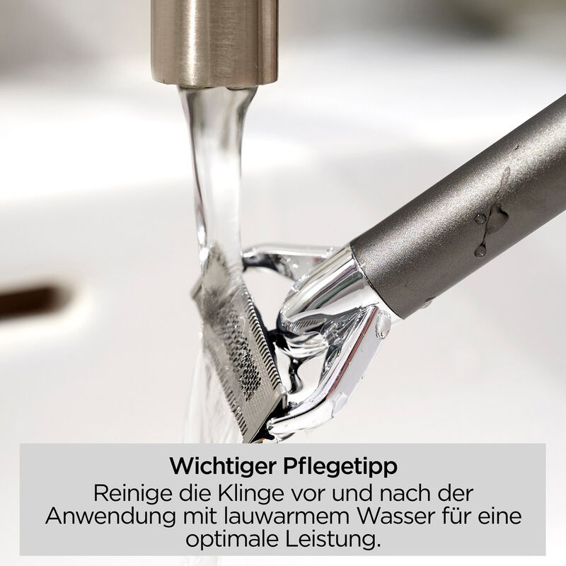 Ein Rasierer wird unter fließendem Wasser gespült. Der Rasierer ist silber und dunkelgrau, Wassertropfen sind sichtbar.