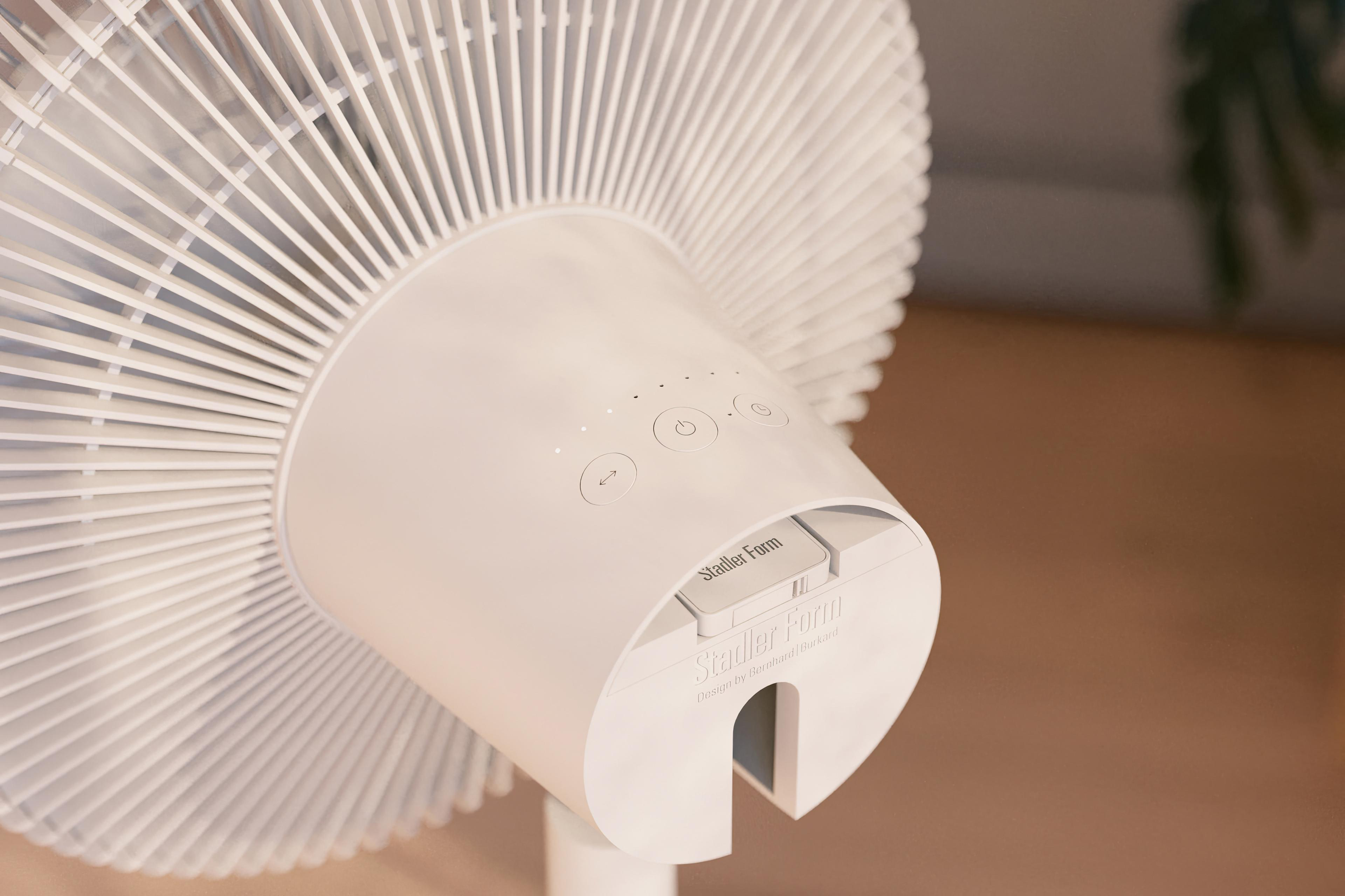 Ein weißer Ventilator mit kreisförmigem Design. Er verfügt über Steuertasten und das Stadler Form Logo. Der Hintergrund ist hellbraun.