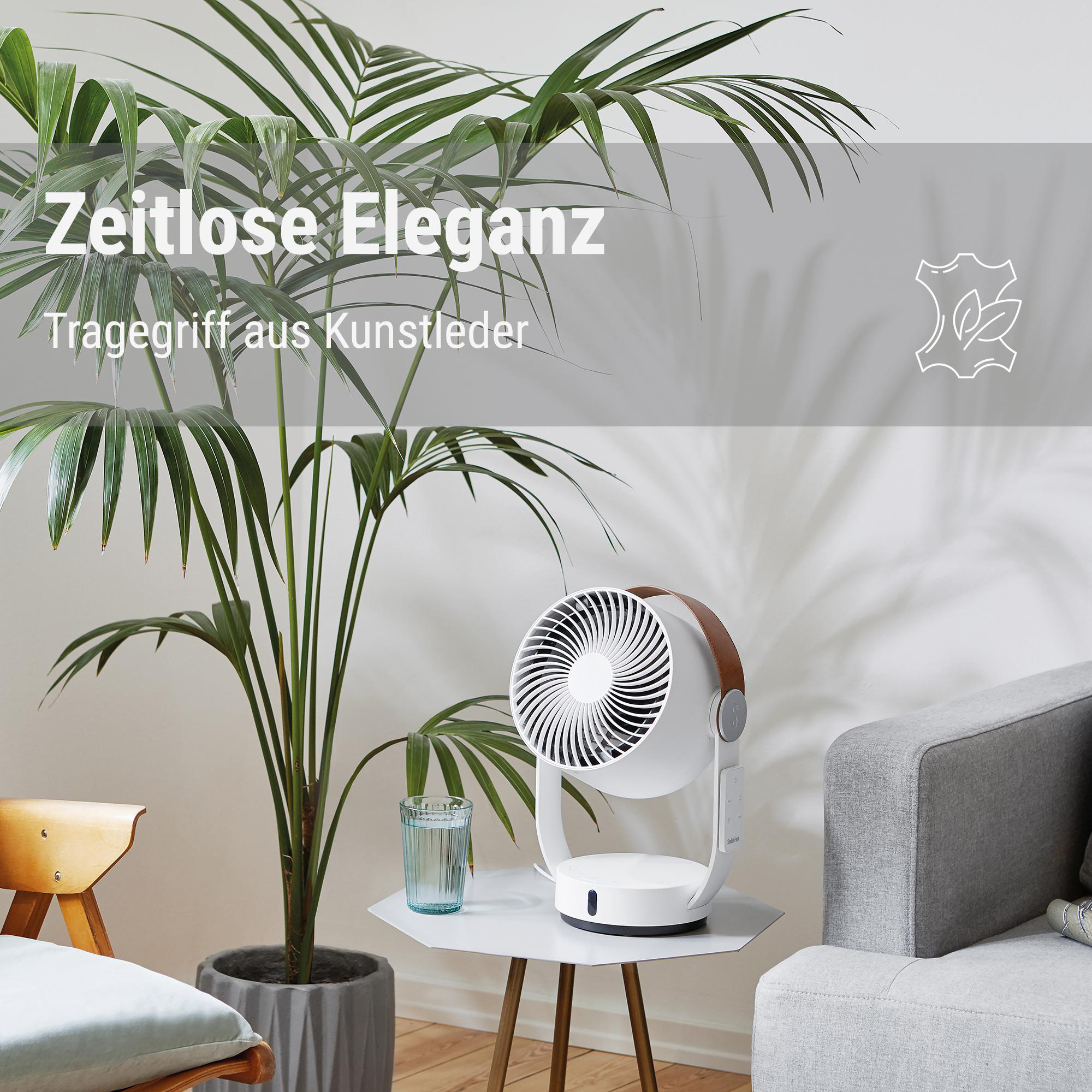 Ein weißer Ventilator mit braunem Griff steht auf einem Tisch. Im Hintergrund ist eine Pflanze. Ein Glas Wasser steht auf dem Tisch.