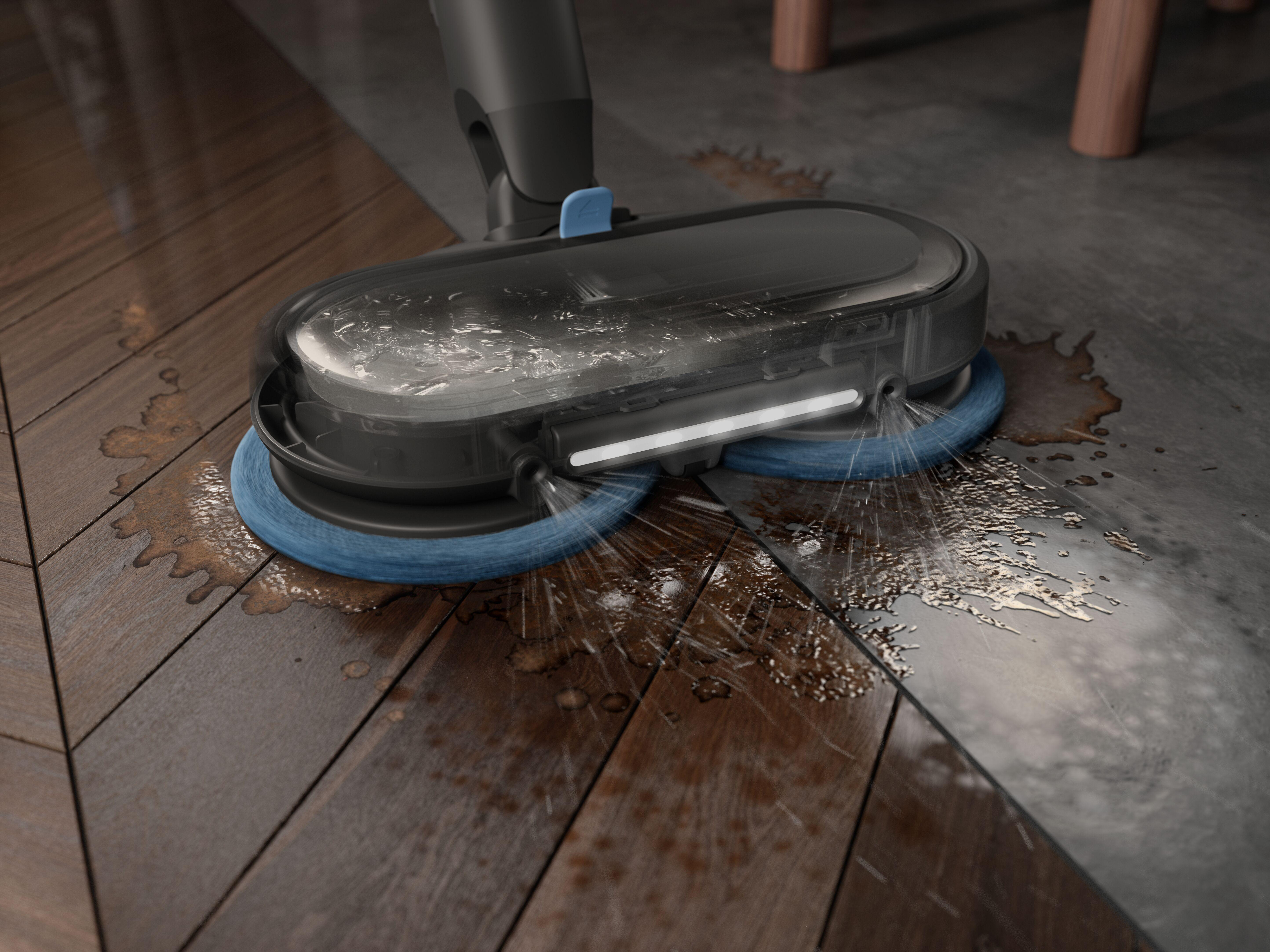 Ein Bodenreiniger sprüht Wasser, während er einen Holzboden reinigt. Der Reiniger hat blaue Pads.