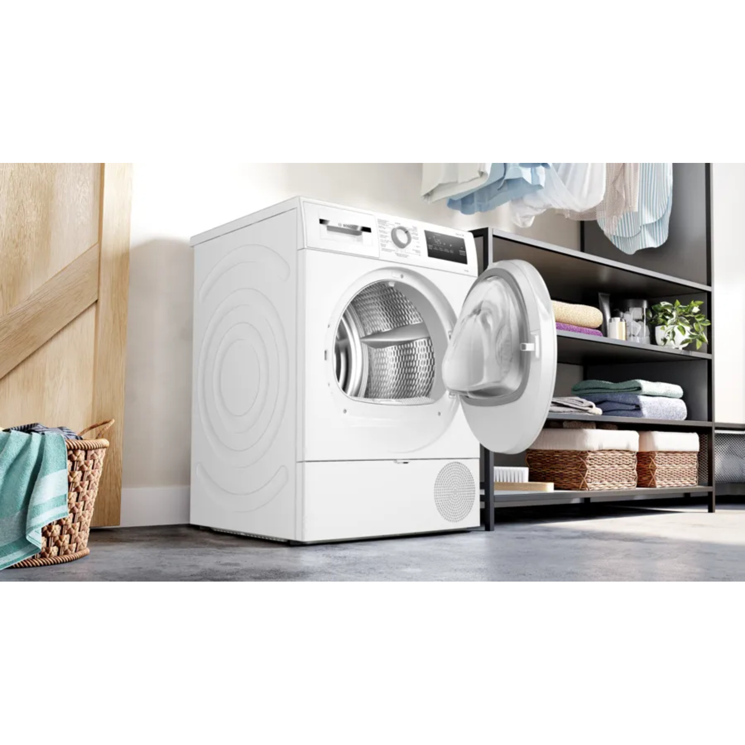 Un sèche-linge blanc avec une porte ouverte. Un panier avec une serviette est à gauche. Des étagères avec des serviettes, des plantes et des paniers à droite.