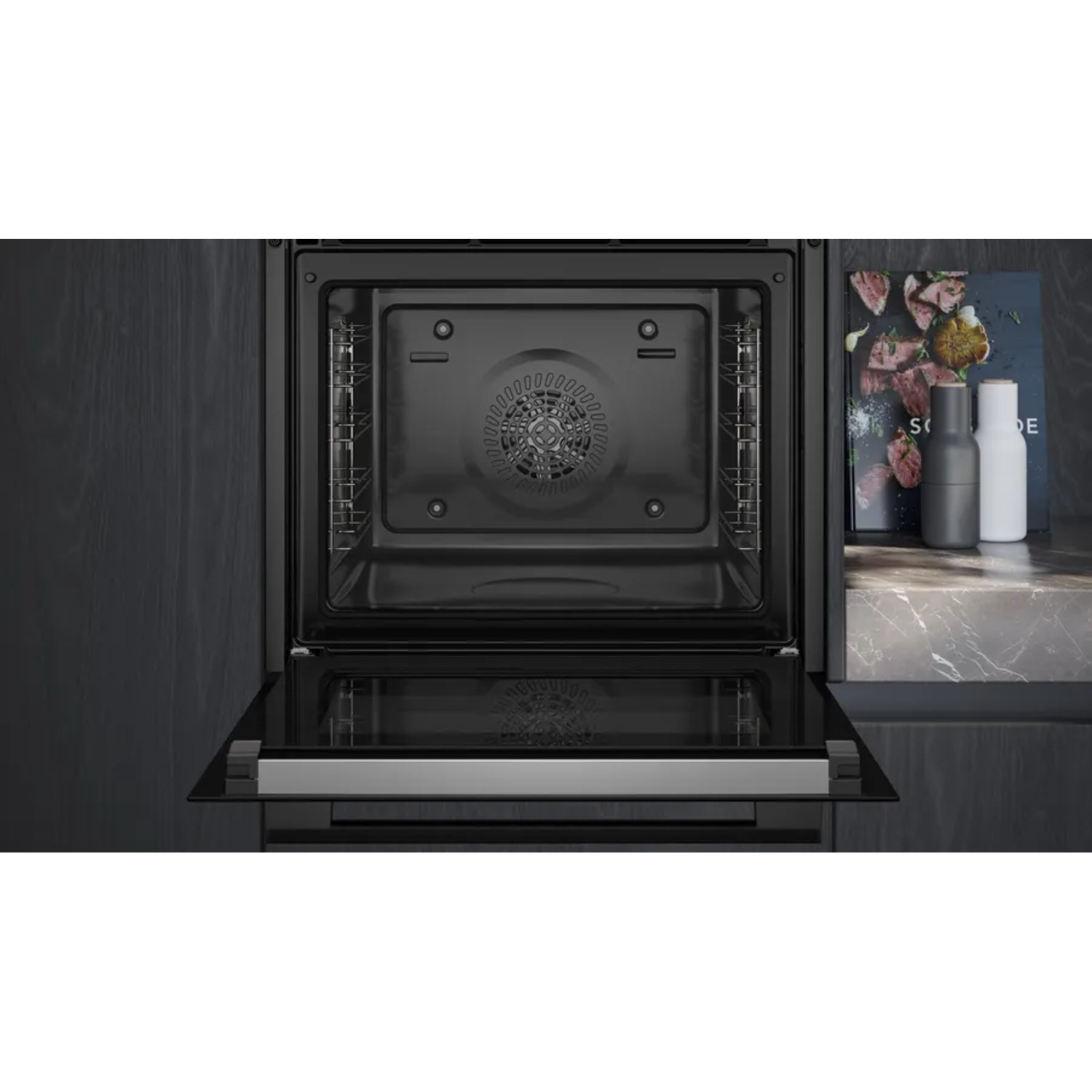 An open black oven with a glass door. A cookbook and salt and pepper shakers sit to the right.