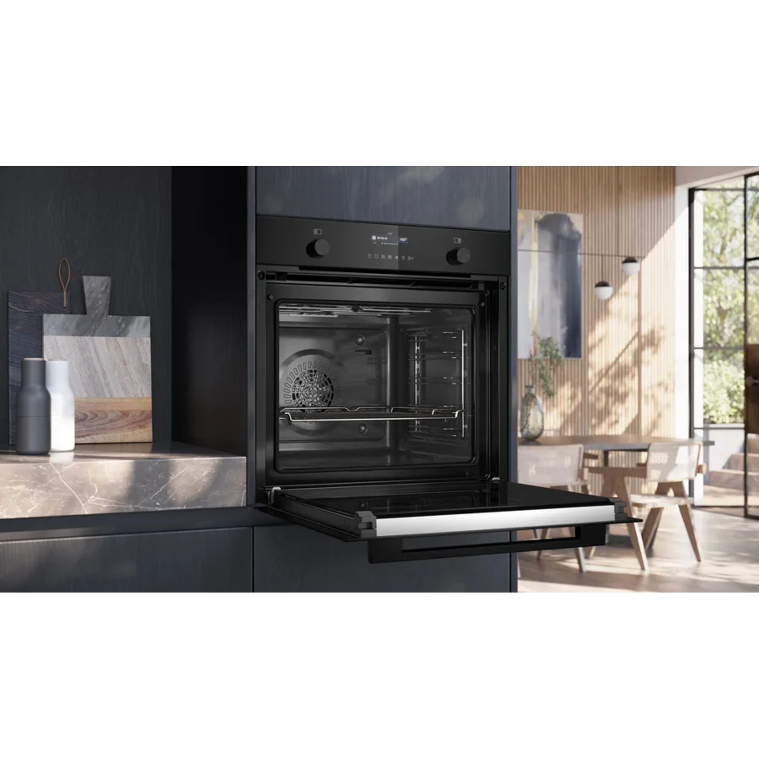 Open oven in a modern kitchen. Dark cabinet, marble countertop, and a dining area with natural light in the background.