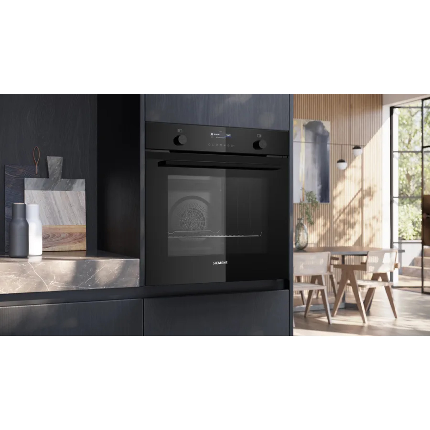 A black oven built into dark cabinetry. A marble countertop and kitchen items are on the left. A dining area is visible.