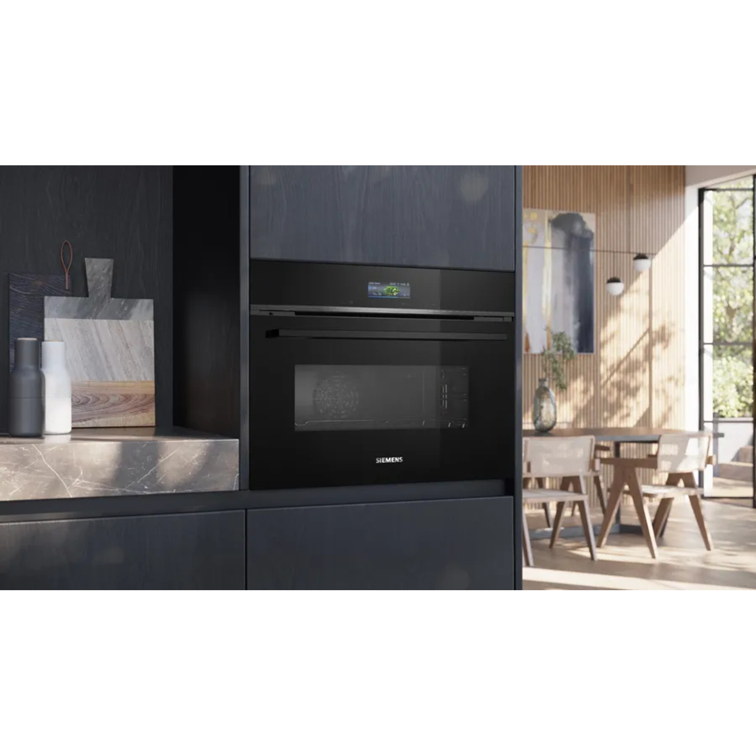 A black built-in oven with a digital display. Kitchen setting with marble countertop, wooden table, and chairs. Natural light.