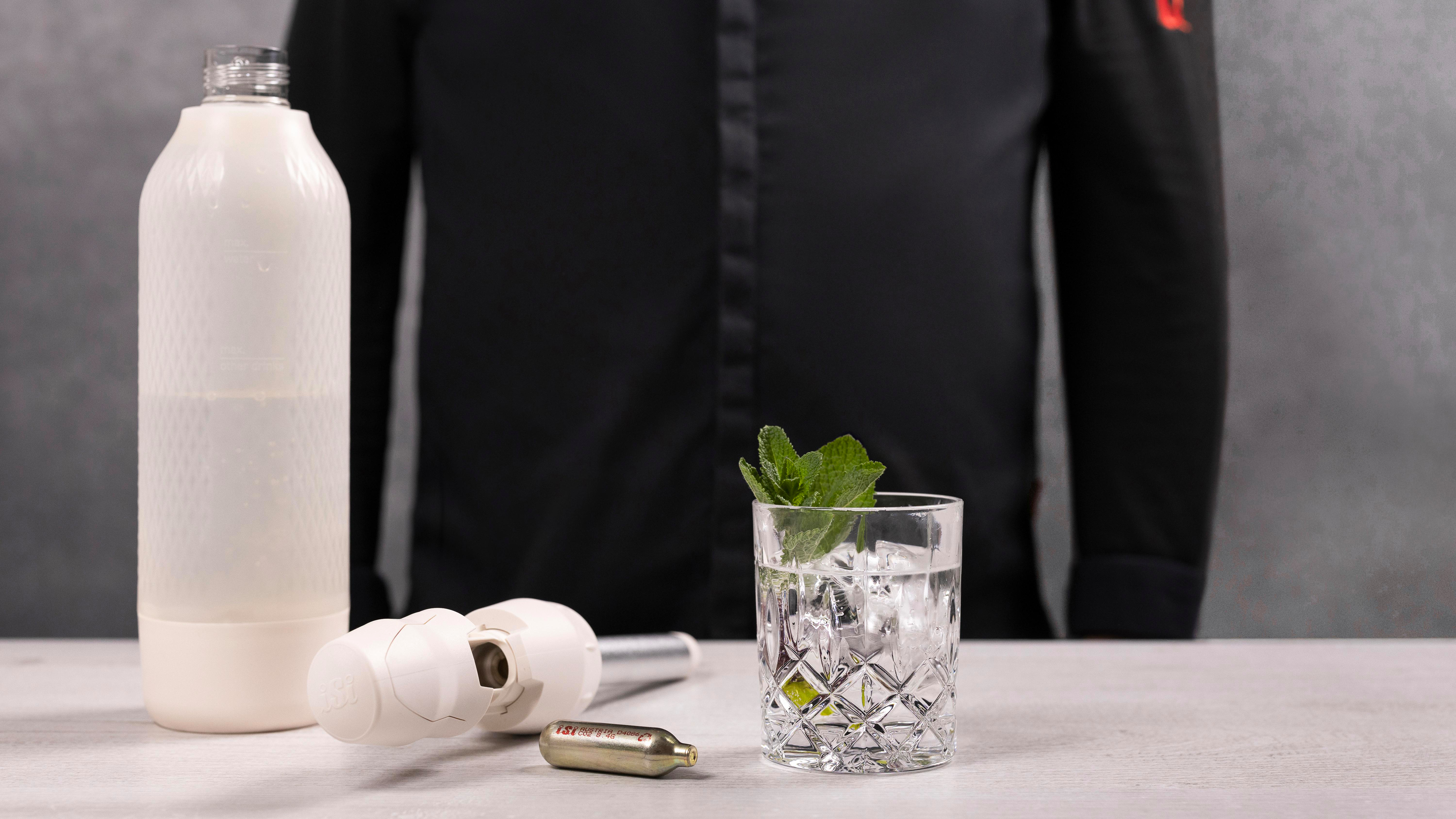 Barszene mit Cocktail, Minze, Eis und Sodabereiter. Eine Person in schwarzer Kleidung ist im Hintergrund.
