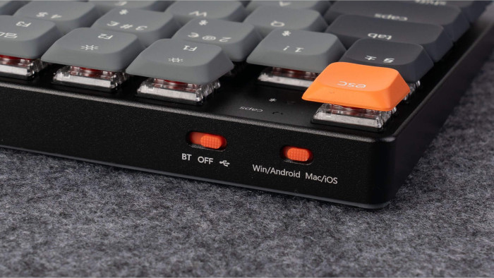 Nahaufnahme einer schwarzen mechanischen Tastatur mit grauen Tasten, einer orangefarbenen Esc-Taste und zwei orangefarbenen Schaltern.