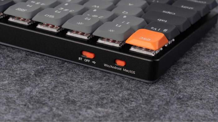 Nahaufnahme einer mechanischen Tastatur. Die Tastatur hat graue Tasten, einen schwarzen Rahmen und eine orangefarbene Escape-Taste und Schalter.
