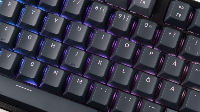 Nahaufnahme einer schwarzen Tastatur mit beleuchteten Tasten. Buchstaben und Zahlen sind auf den Tasten zu sehen, mit lila und blauer Beleuchtung.