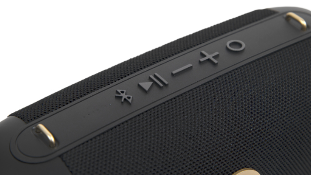 Zbliżenie czarnego głośnika z przyciskami sterowania, w tym odtwarzanie/pauza, głośność i Bluetooth. Widoczne złote akcenty i tekstura siatki.