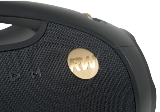 Zbliżenie czarnego głośnika z uchwytem. Posiada złote logo i siatkowy przód. Tło jest białe.