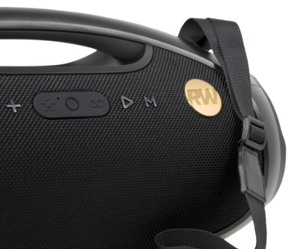 Czarny głośnik z przyciskami i paskiem. Złote logo RW z boku. Przyciski obejmują plus, słońce, koło i odtwarzanie.