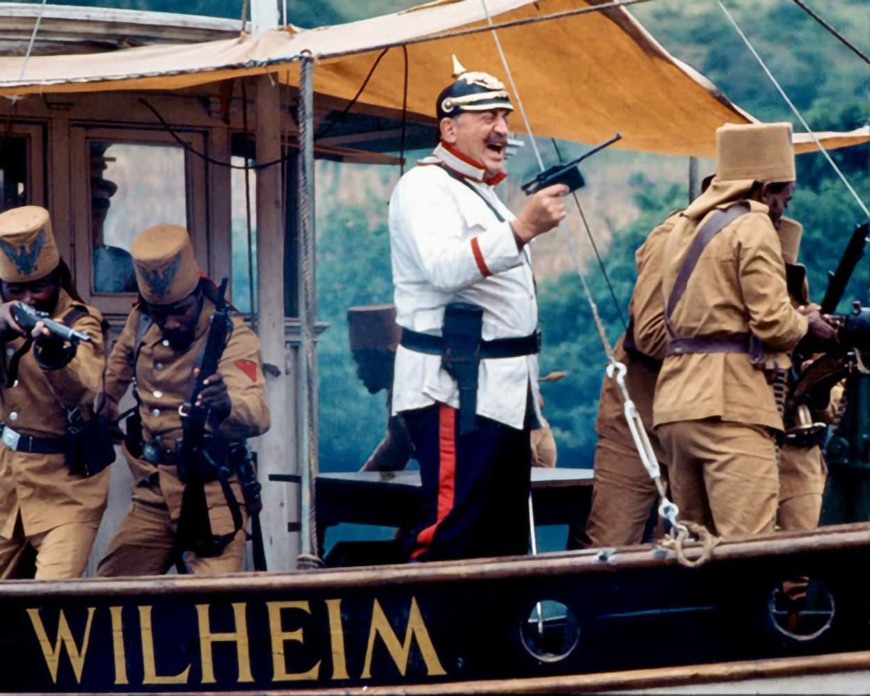 Männer in Militäruniformen auf einem Boot. Ein Mann in weißem Hemd und Helm hält eine Waffe und lächelt. Andere zielen mit Waffen.