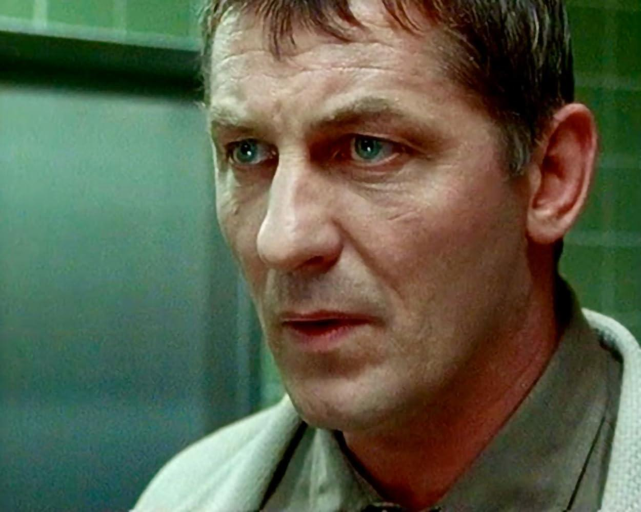 Ein Mann mit kurzen, dunklen Haaren und blauen Augen schaut in die Kamera. Er trägt ein helles Hemd vor grünem Hintergrund.