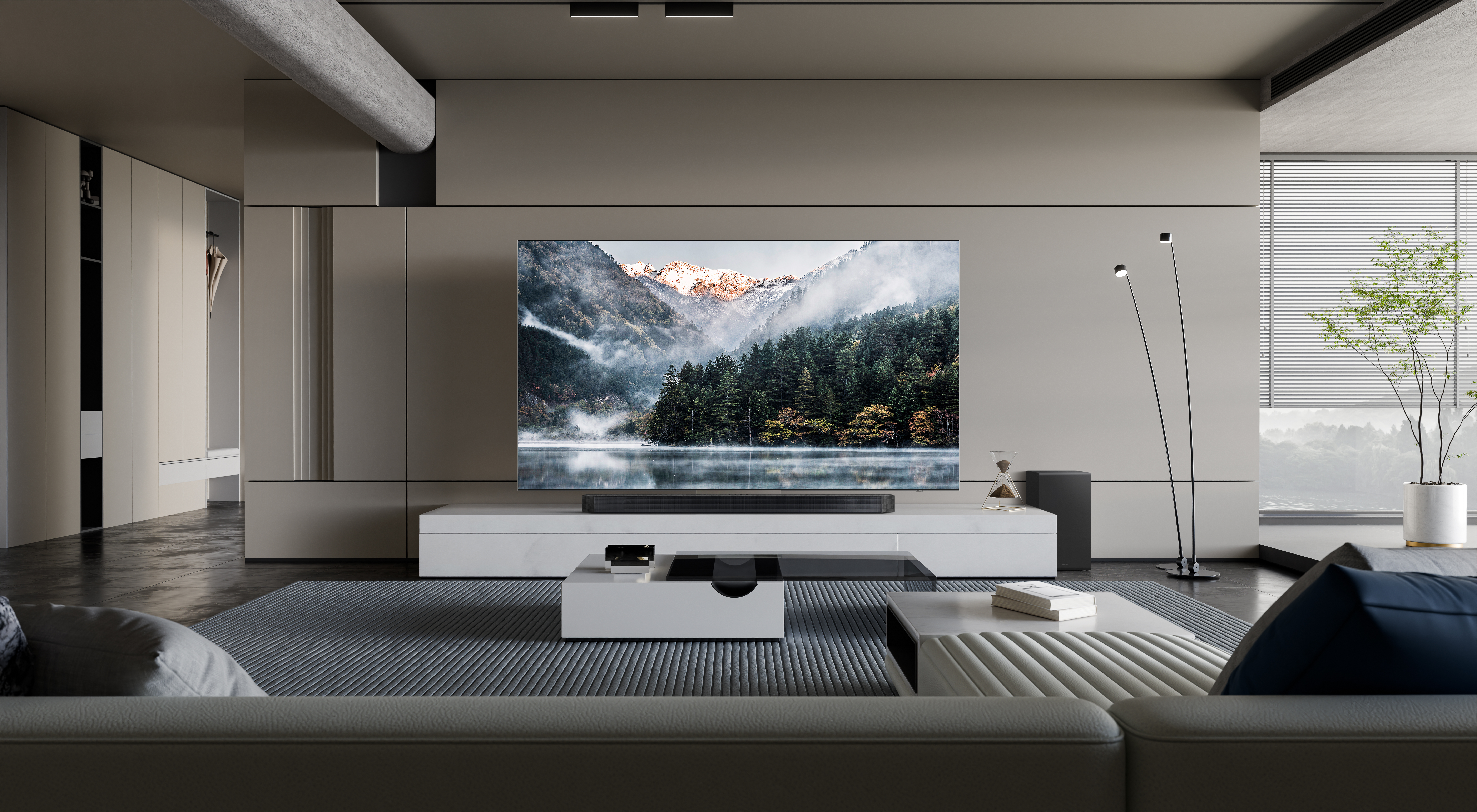 Ein modernes Wohnzimmer mit einem großen Fernseher, der eine Bergseeszene zeigt. Ein weißer Couchtisch und ein graues Sofa sind im Vordergrund.