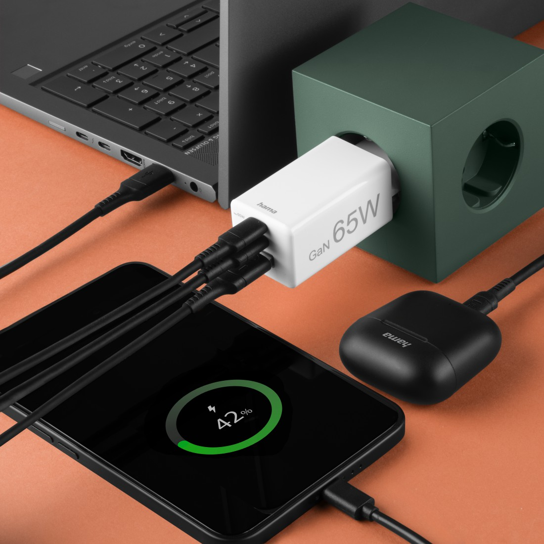 Ein Telefon, das zu 42 % aufgeladen wird, mit einem weißen Ladegerät, einem Laptop und Ohrhörern. Alles ist mit schwarzen Kabeln verbunden.