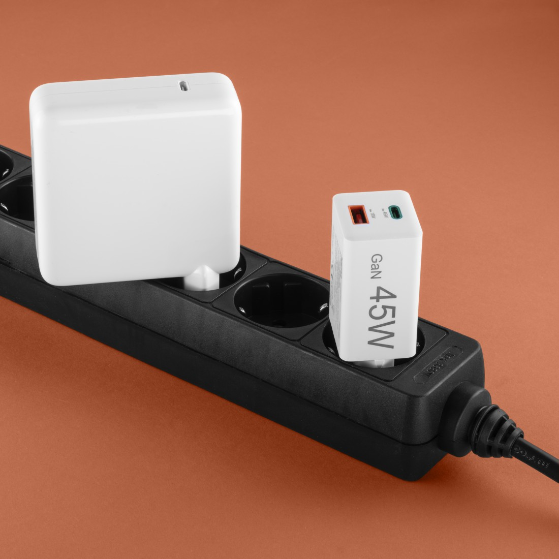 Zwei weiße Netzadapter stecken in einer schwarzen Steckdosenleiste vor orangefarbenem Hintergrund. Ein Adapter hat 45W.