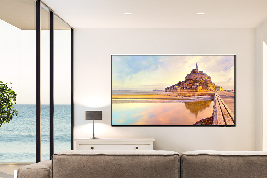 Un soggiorno con una grande TV che mostra una scena di castello. Divano e finestre con vista mare in primo piano.