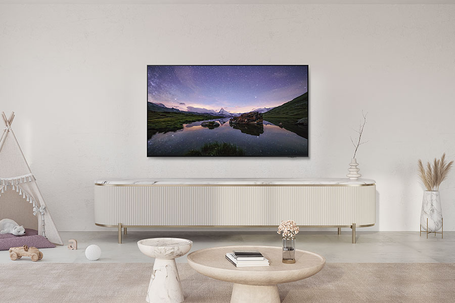 Un televisore mostra un cielo stellato sopra un lago e montagne. Sotto, un mobile bianco, tavoli e decorazioni sono disposti in una stanza.