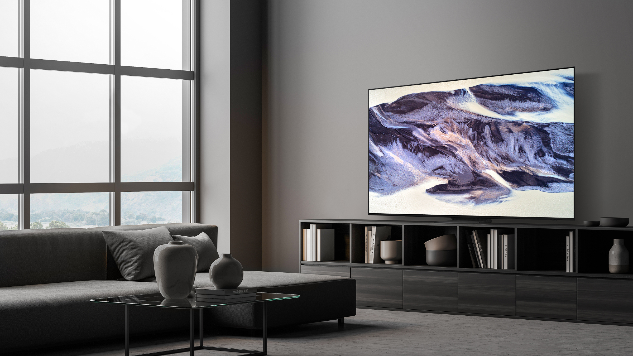 Soggiorno moderno con divano grigio, tavolino in vetro, TV con paesaggio e grande finestra con vista montagne.