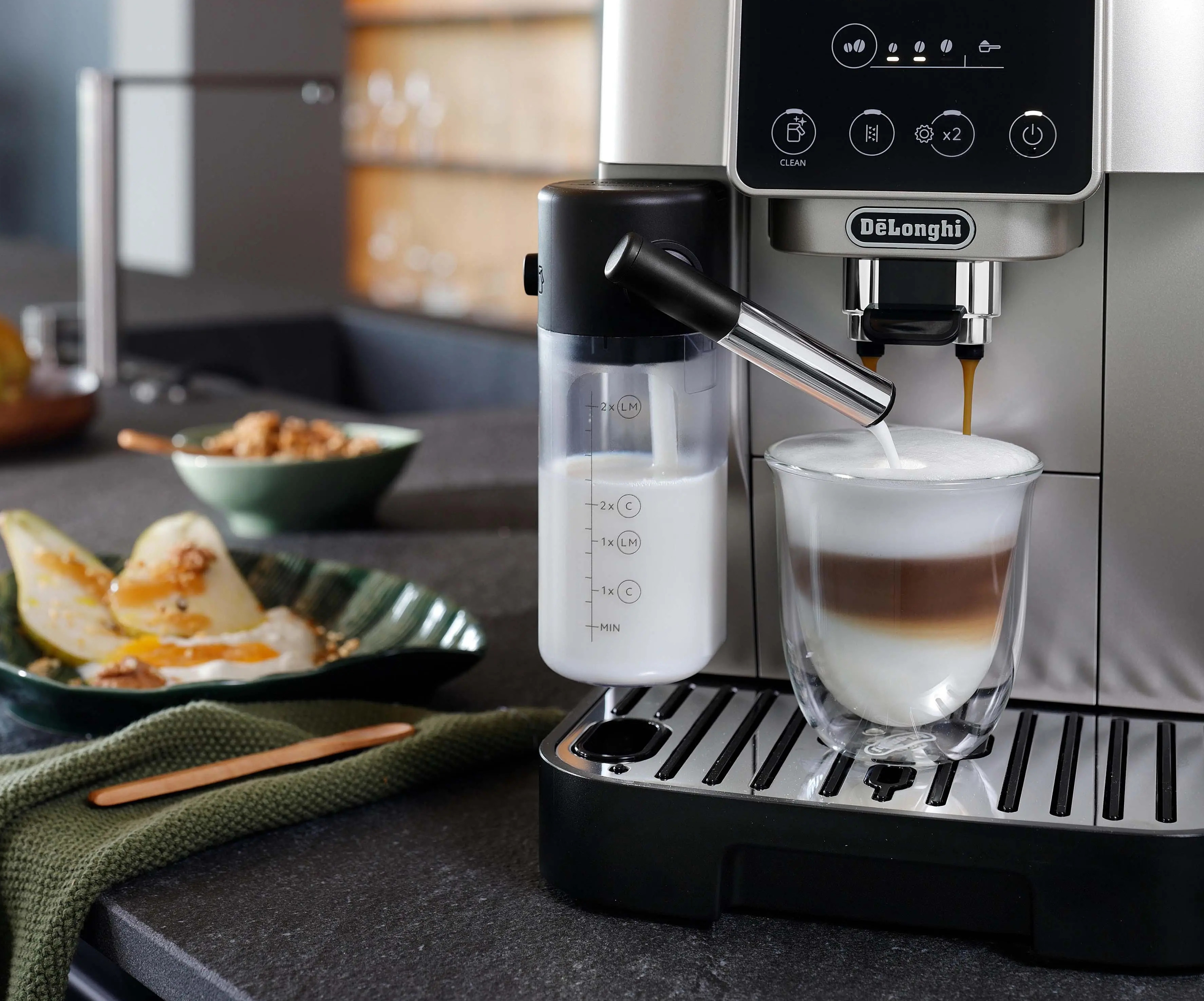 Ekspres do kawy wlewa pianę mleczną do szklanki. Owoce są obok.