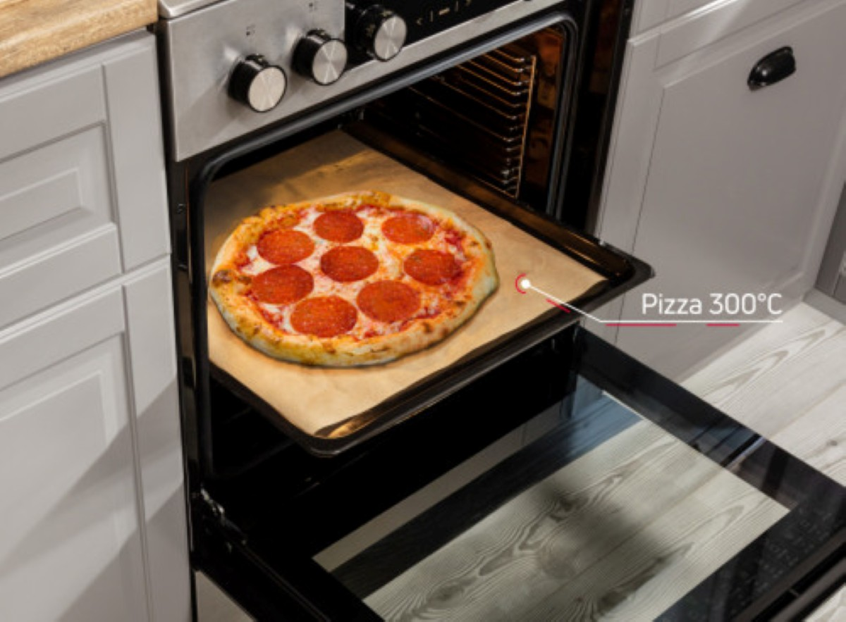 Pizza z pepperoni piecze się w piekarniku w temperaturze 300°C. Drzwi piekarnika są otwarte, widać pizzę na tacy.