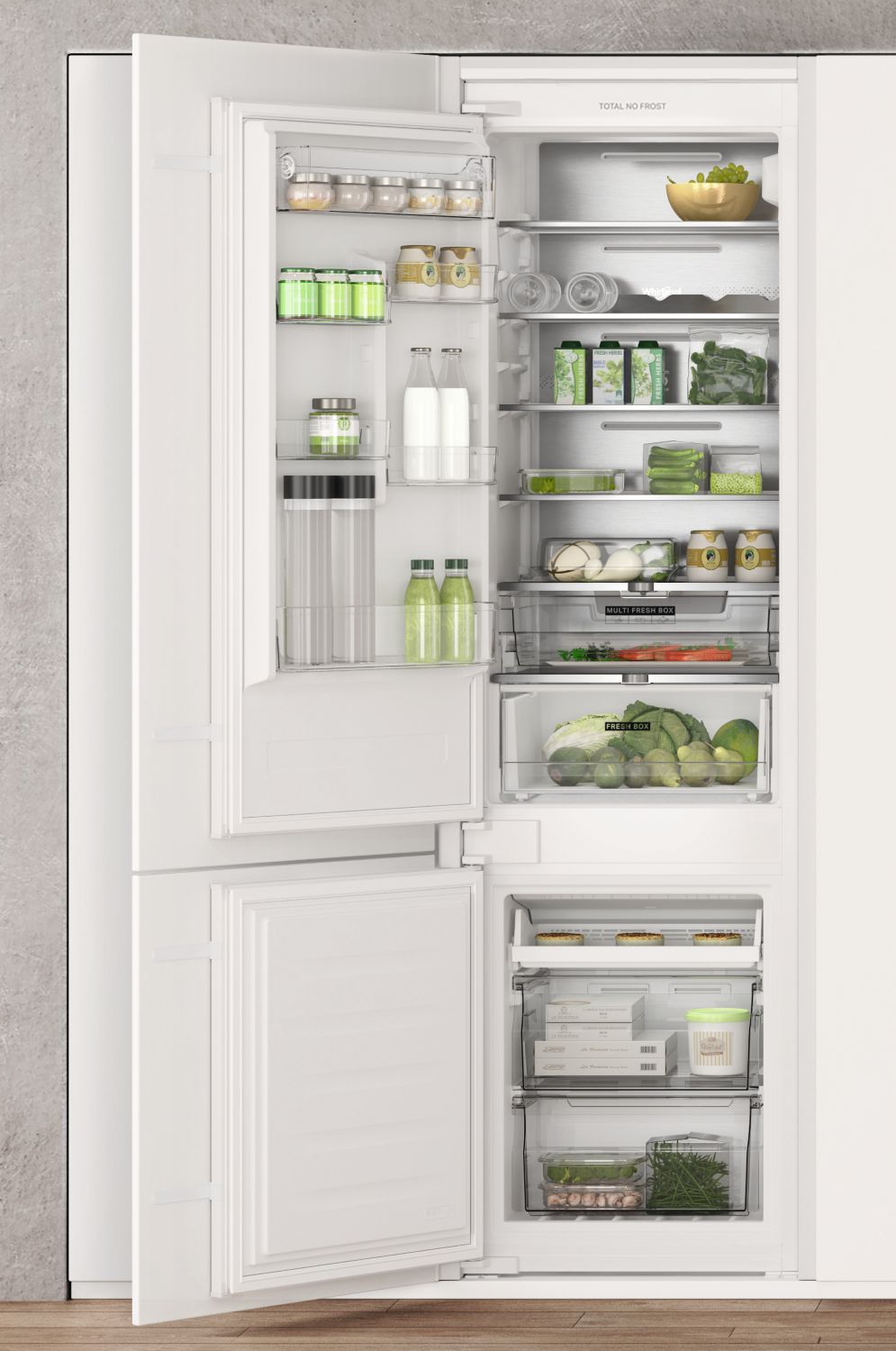 Refrigerador blanco abierto lleno de comida. Artículos visibles: frascos, botellas, verduras, frutas y recipientes. Compartimento del congelador abierto.