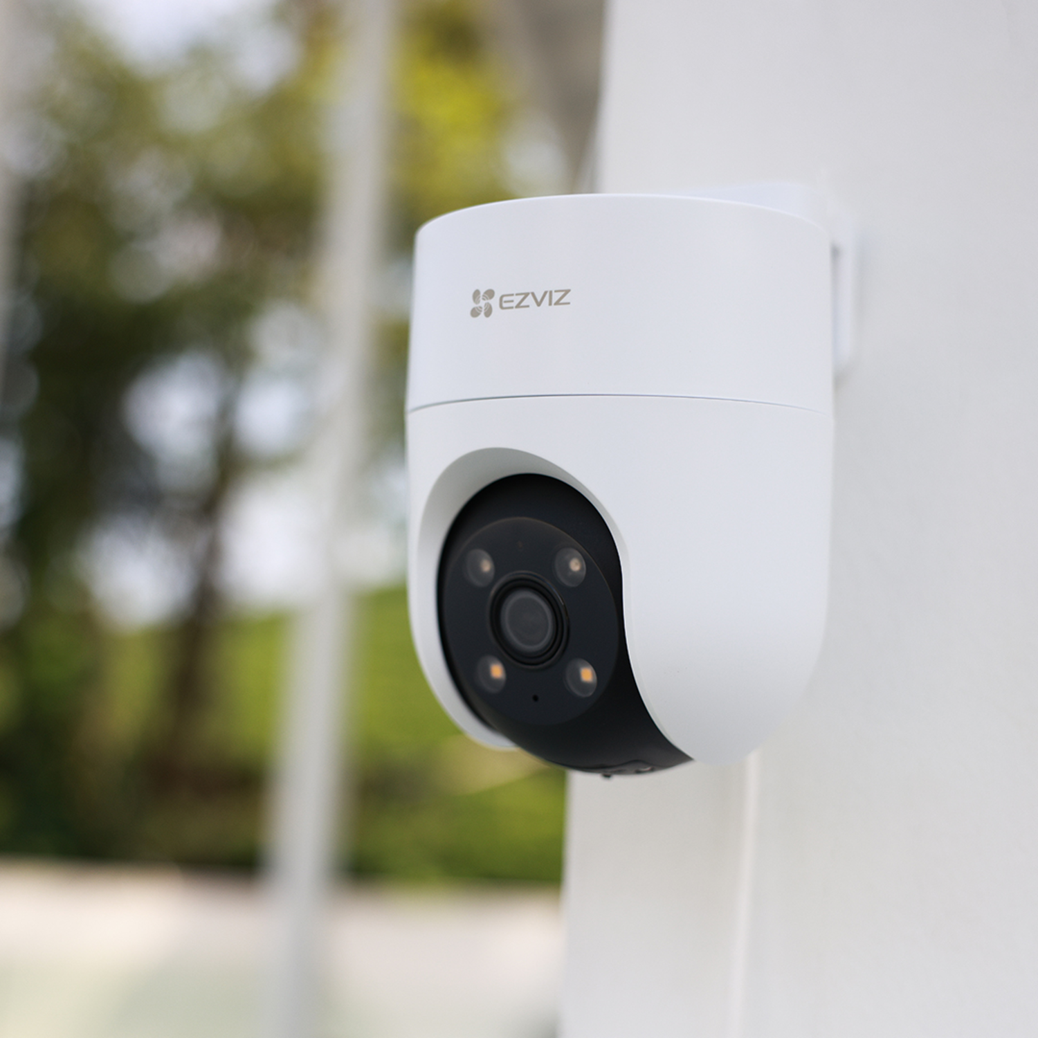 A white EZVIZ security camera mounted on a white surface. Camera has a black lens and is pointed forward. Green background.