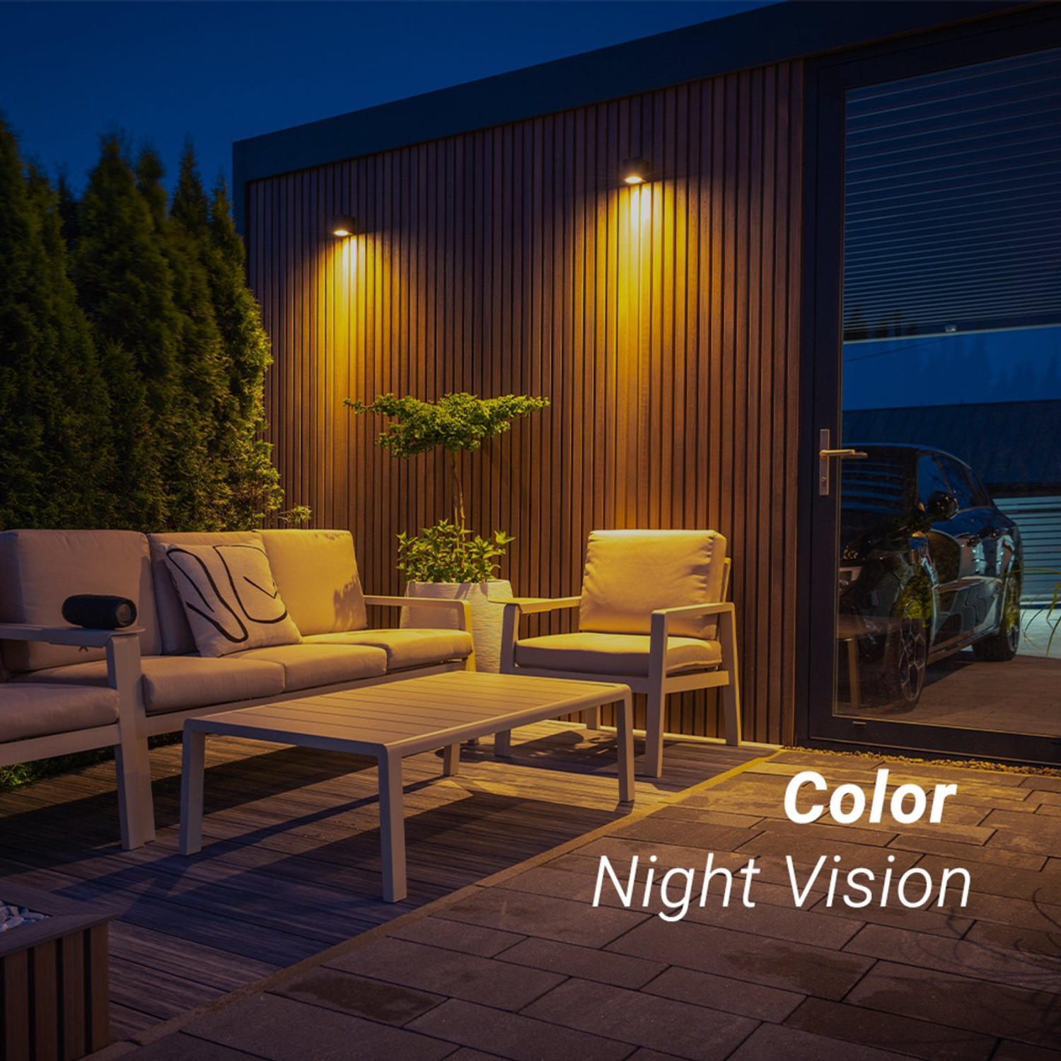 Night scene with patio furniture, lights, and a car reflected in a glass door. Dark blue sky. Wooden wall.